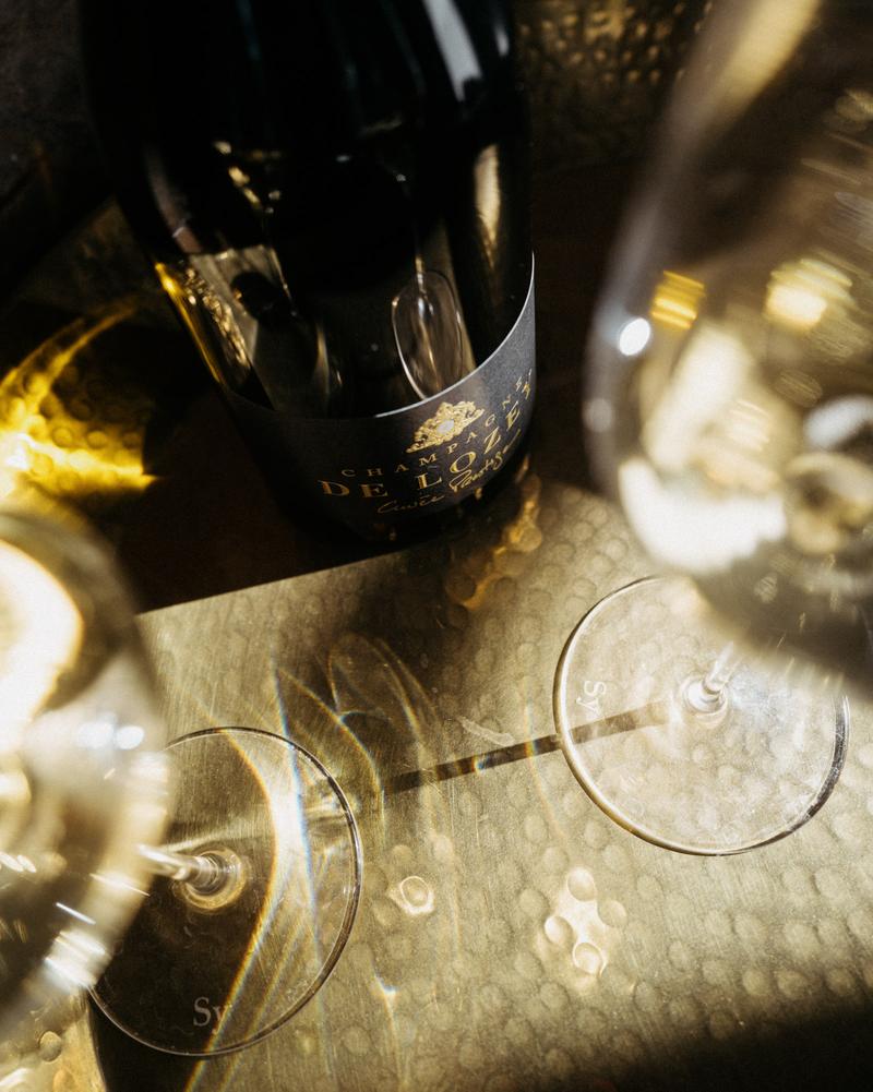 Bottle of Champagne De Lozey Cuvée prestige sitting on golden plate between two Champagne glasses
