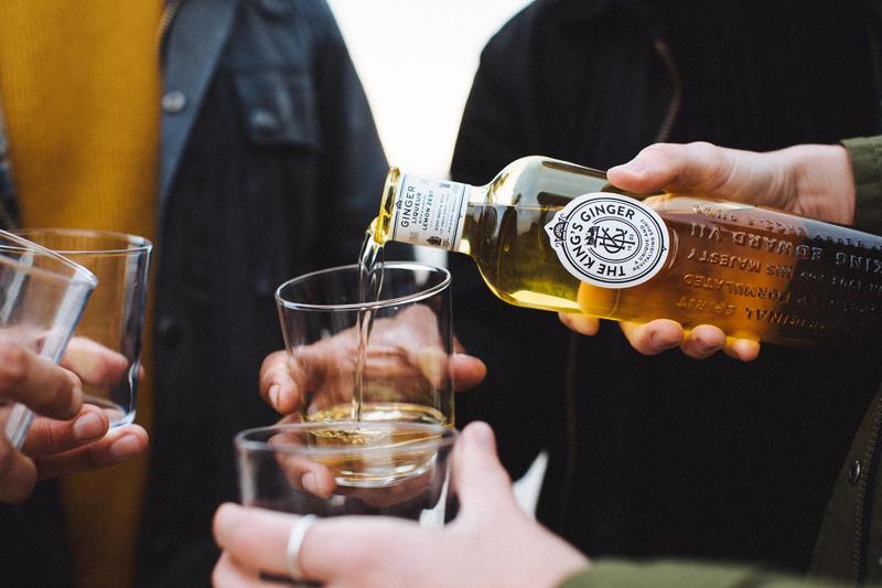 Close up of a hand pouring The King's Ginger into a three hands holding empty glasses