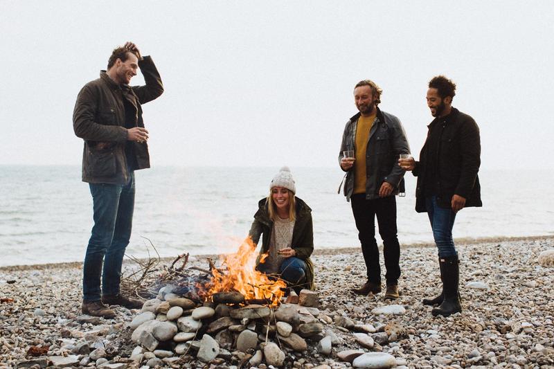 A group of friends gathered around a campfire on the beach enjoying a glass of The King's Ginger