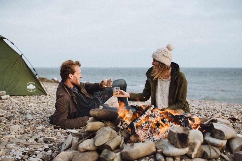 A couple enjoying a glass of The King's Ginger on the beach in front of a campfire