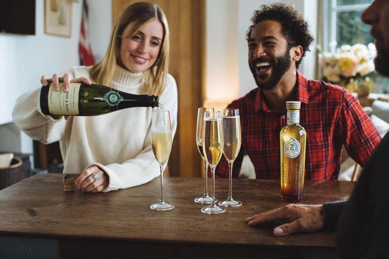 Scene of friends at a country table pouring Berry Bros & Rudd champagne into a glass next to a bottle of King's Ginger