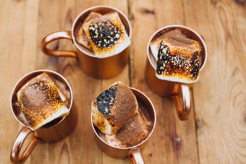 Top shot of four copper mugs of hot chocolate each topped with a big marshmallow