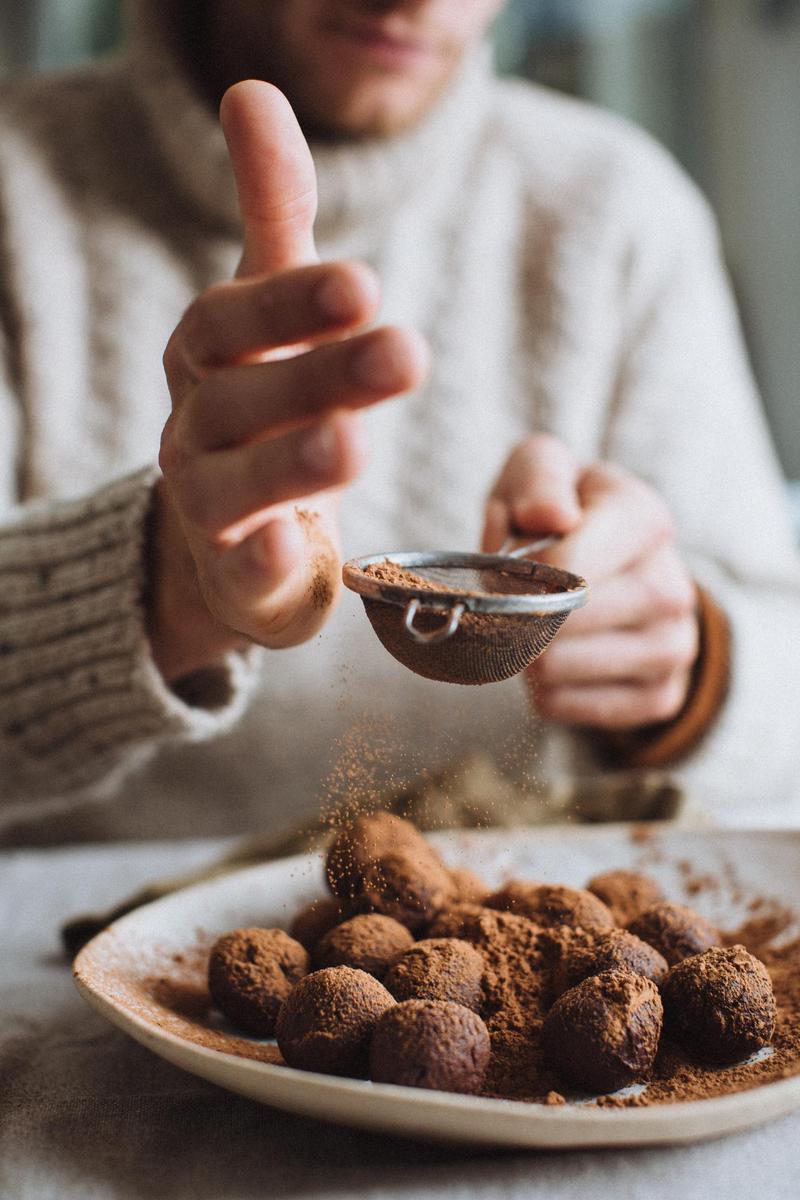 Close up of a hand tapping a small sieve to sprinkle chocolate powder onto homemade truffles