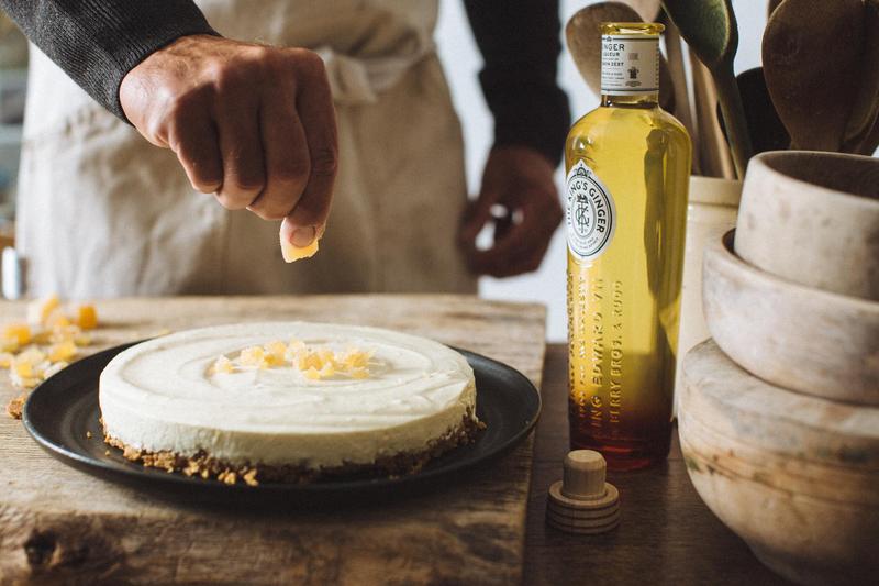 A hand placing a piece of candied ginger on a homemade tart next to a bottle of The King's Ginger