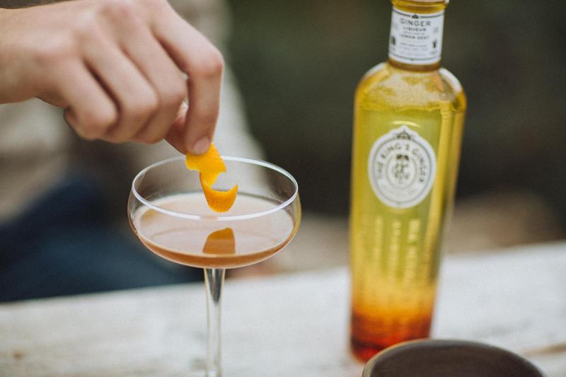 Close up of hand placing orange zest onto a King's Ginger cocktail