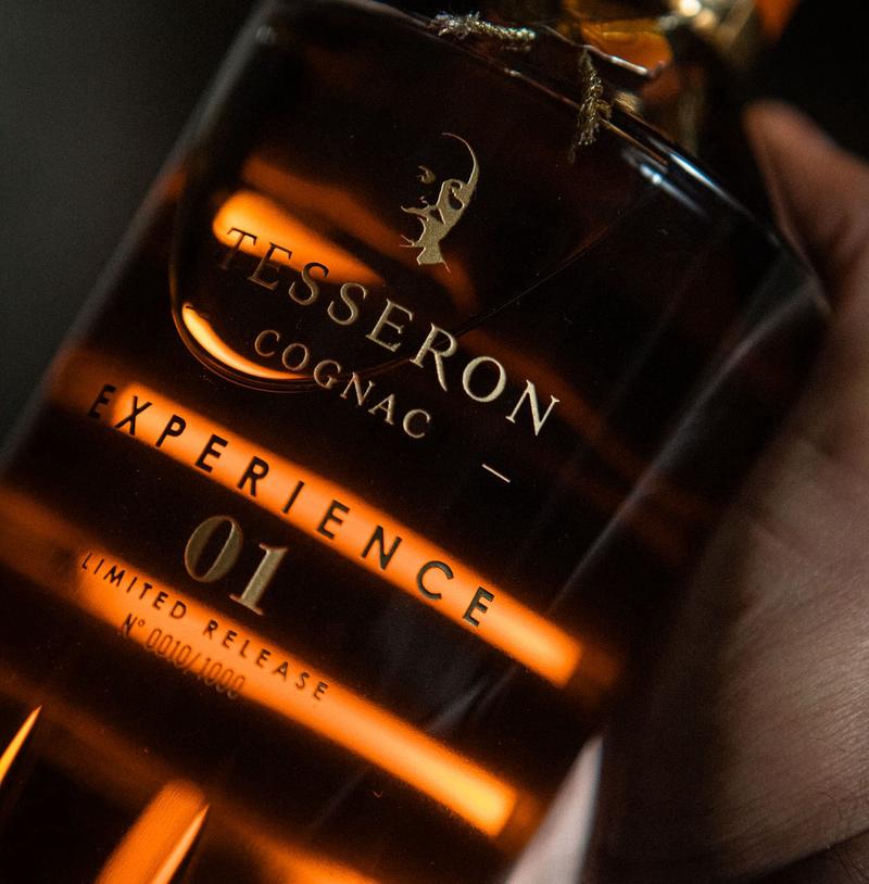 Close up of hand holding a bottle of Cognac Tesseron Experience 01 with light shining through the liquid